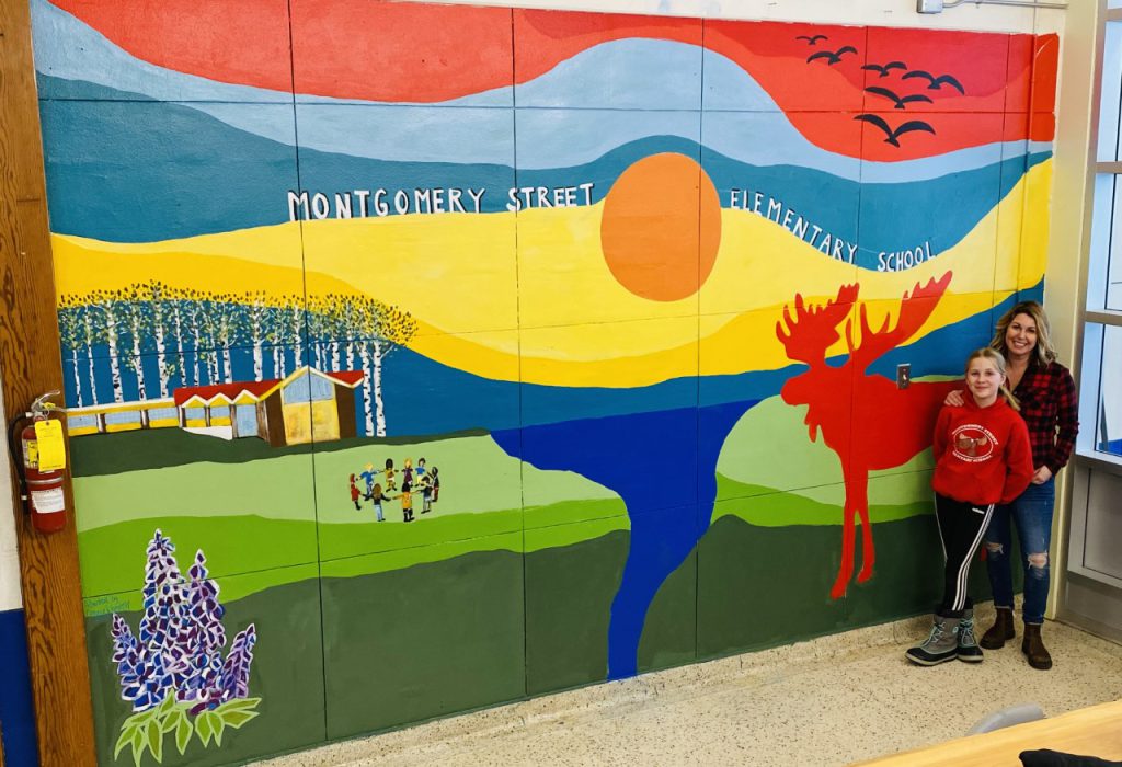 Artist Connie Wheaton and a student helper at the new mural she painted in the Montgomery Street Elementary School front entrance.