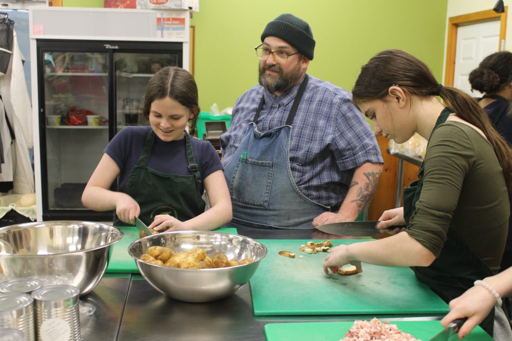 Greener Village chef Yves Dechaine works in the kitchen with Devon Middle School Grade 7 students Wara Sebastian and Sierra Bourgoin during the students' visit on April 17, 2024.