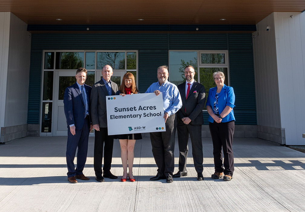 (L-R) David McTimoney, superintendent of Anglophone West School District; Thomas Geburt, chair of the district education council; Education and Early Childhood Development Minister Claire Johnson; Jason Burns, principal; Luke Randall, minister responsible for economic development and small business; and Darla Day, the district’s director of schools, in front of the district's newest school, Sunset Acres Elementary School. Photo Credit: GNB